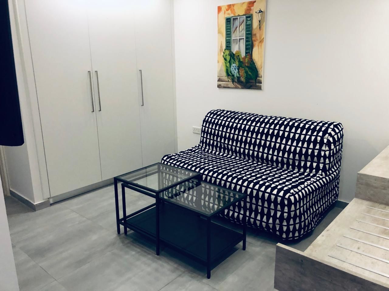 Uma sala de estar com um sofá estampado, uma mesa de centro de vidro e um guarda-roupa.