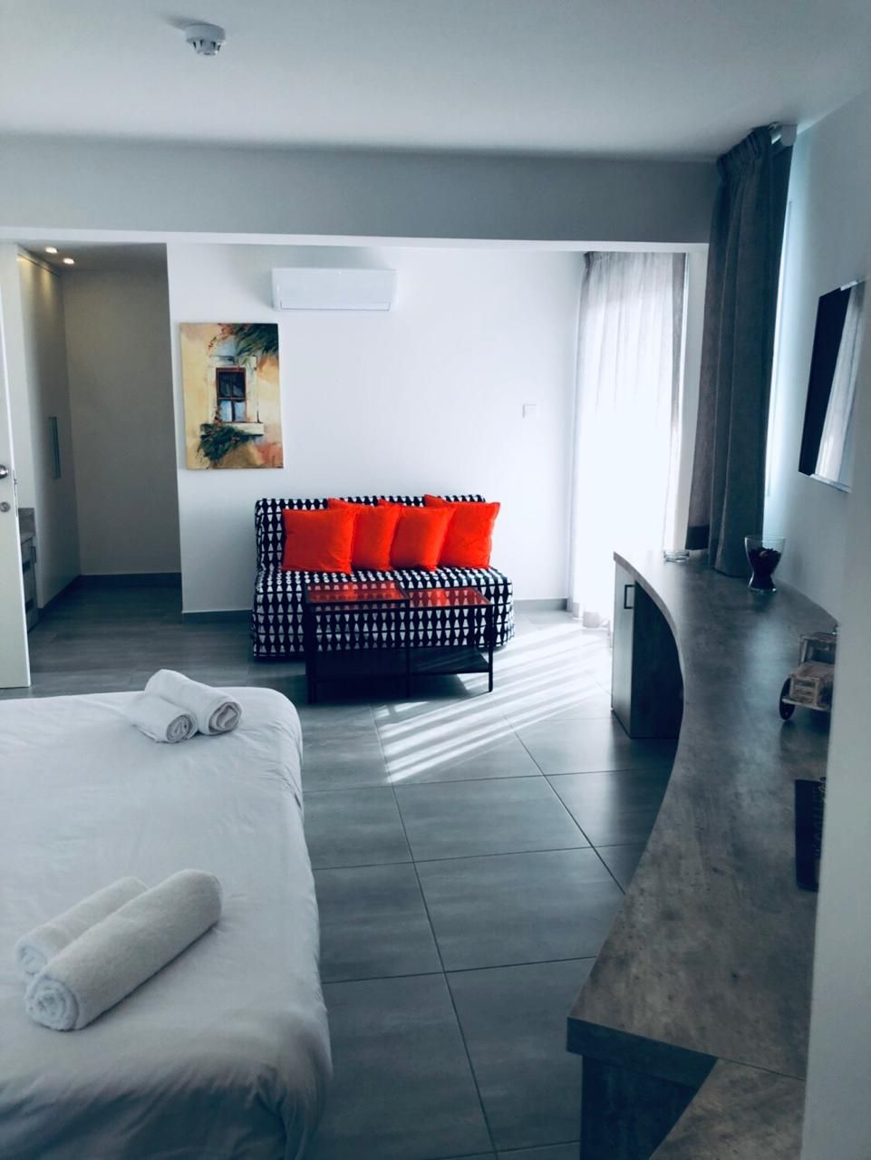 A hotel room with a bed, a seating area with a patterned sofa, and a small kitchenette.
