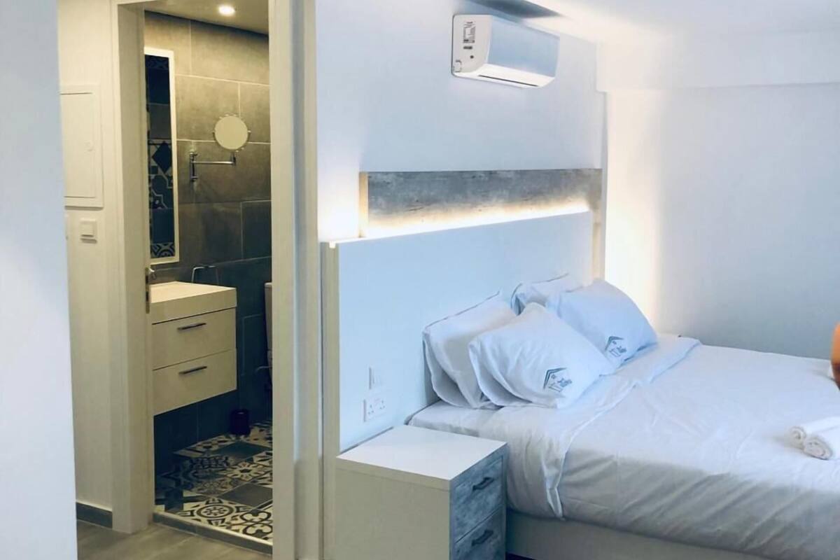 Quarto moderno com cama, mesas de cabeceira, uma mesa redonda de vidro e área de chuveiro.