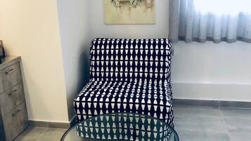 A living room with a patterned sofa, a glass coffee table, and a painting on the wall.