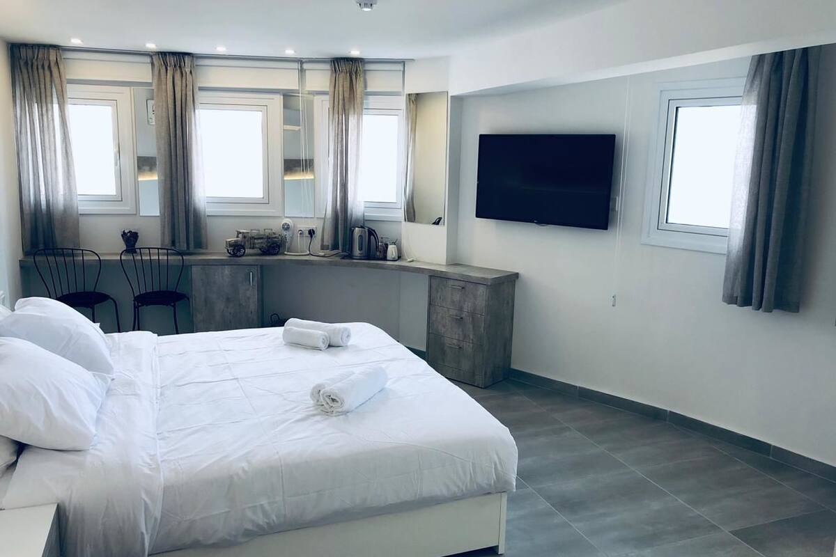 Quarto de hotel moderno com cama grande, escrivaninha, televisão de tela plana e uma janela ampla.