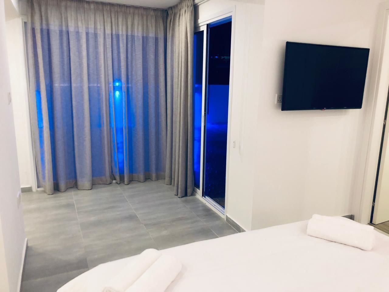 A hotel room with a bed, a TV mounted on the wall, and a sliding glass door leading to a balcony.