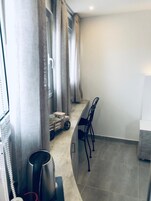 Una habitación pequeña y estrecha con kitchenette, una ventana con cortinas y una zona de estar con sillas.