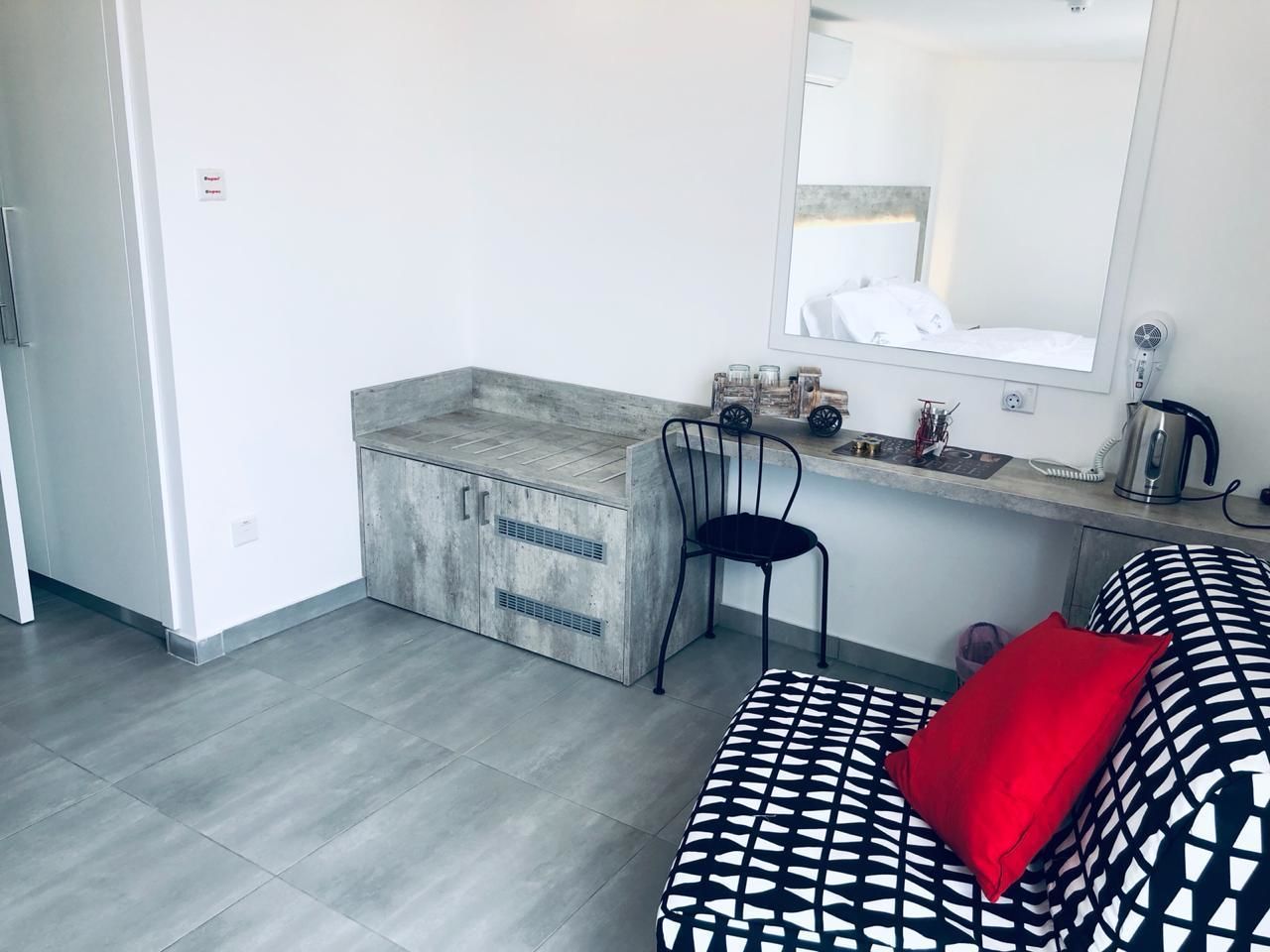 Una habitación compacta con kitchenette, una silla, cama con ropa de cama estampada y un espejo grande.