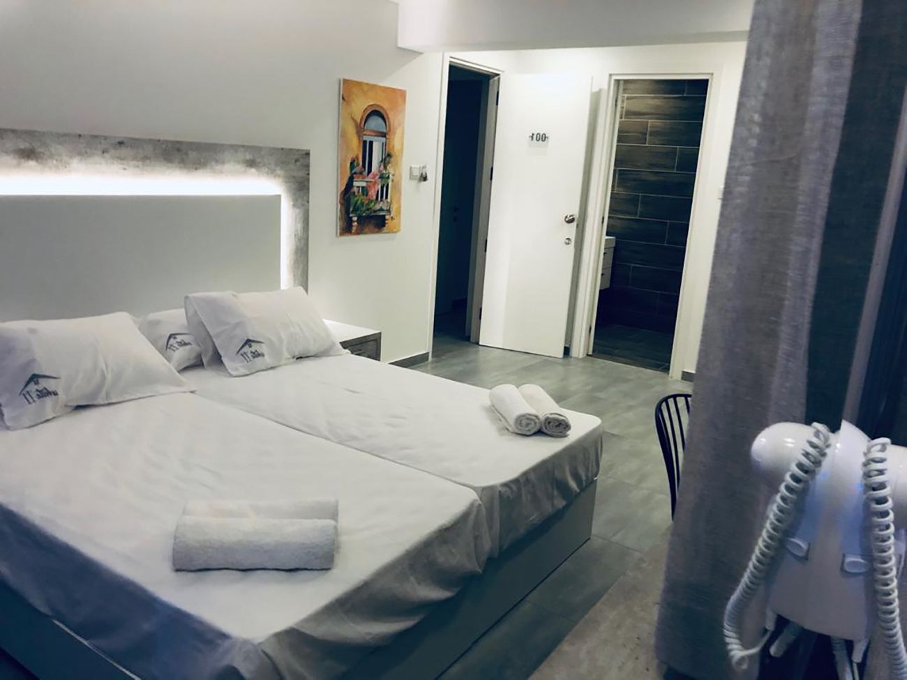 A hotel room with a large bed, a bedside table, a phone, and a painting on the wall.