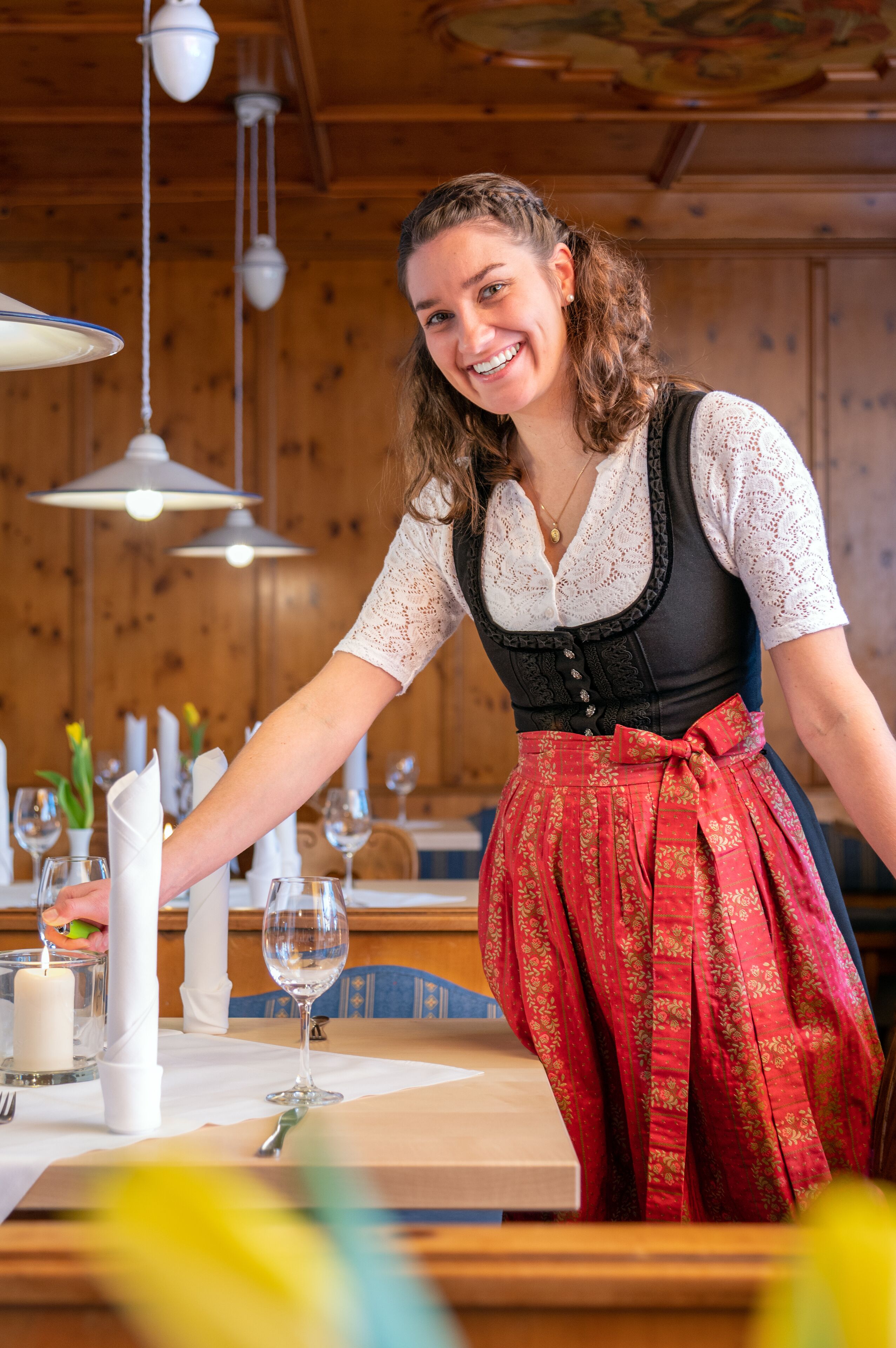 A person in traditional attire serving at a wooden table with candles and wine glasses.