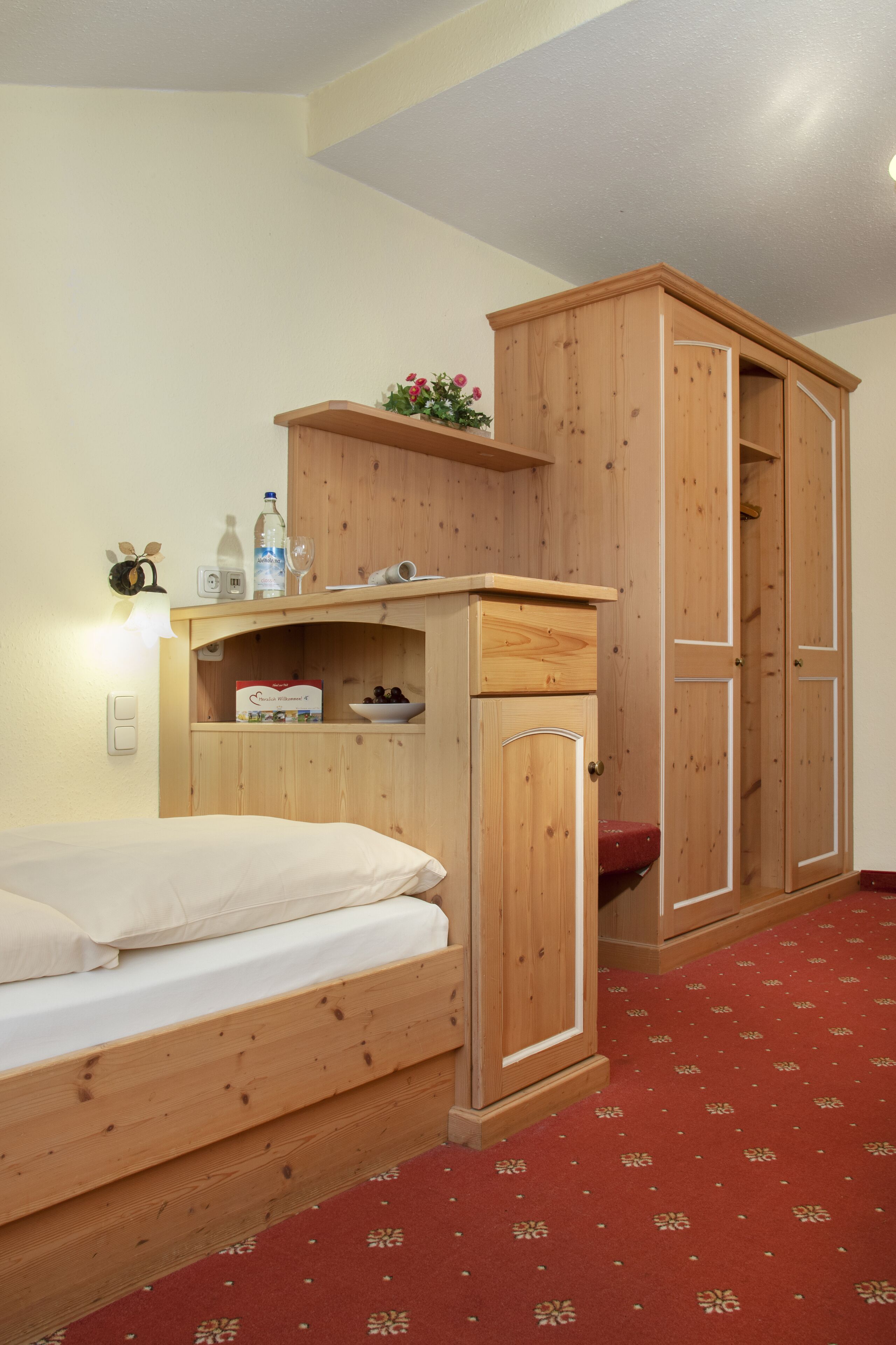 Een slaapkamer met een houten bed, een klein bureau met een lamp en een kledingkast.
