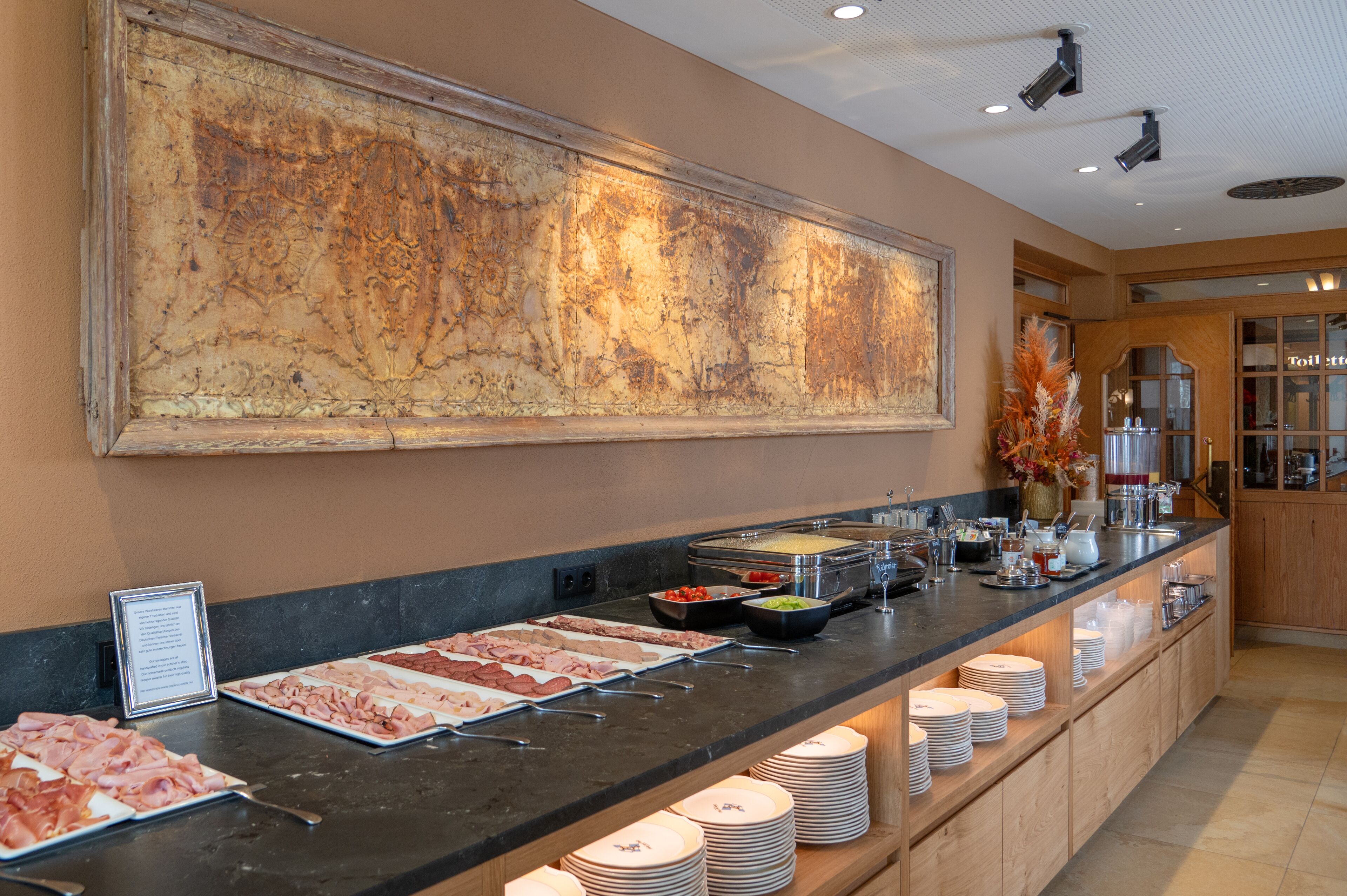 A buffet with various food options and a large abstract painting on the wall.