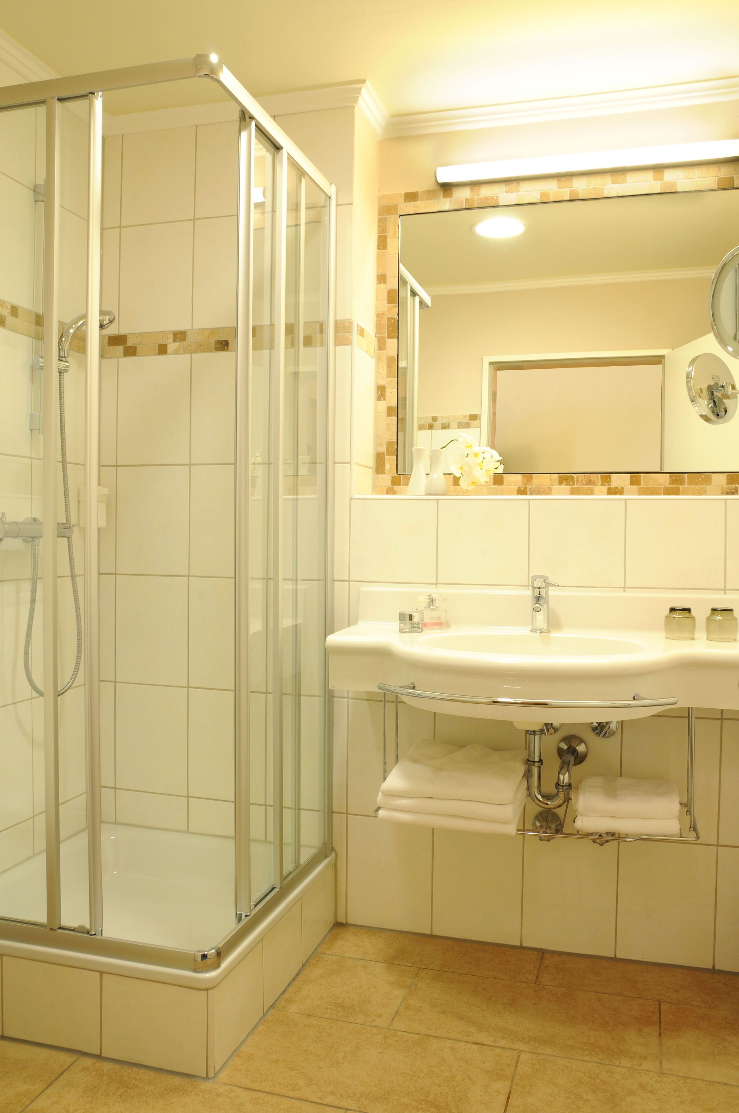 Un baño con cabina de ducha de vidrio, un lavabo con espejo y suelo de baldosas.