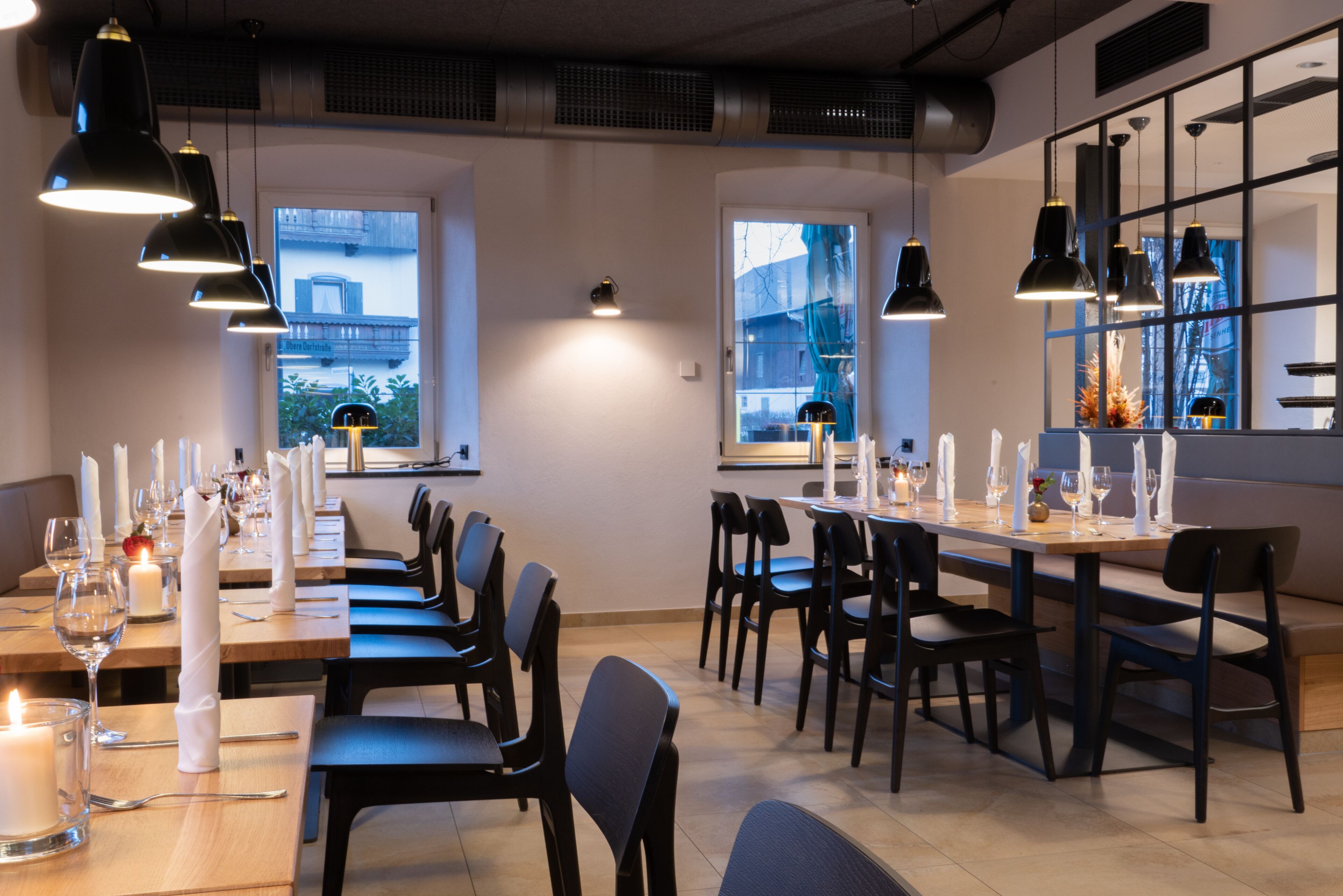 Un restaurante con mesas largas dispuestas para comer, sillas negras e iluminación colgante.