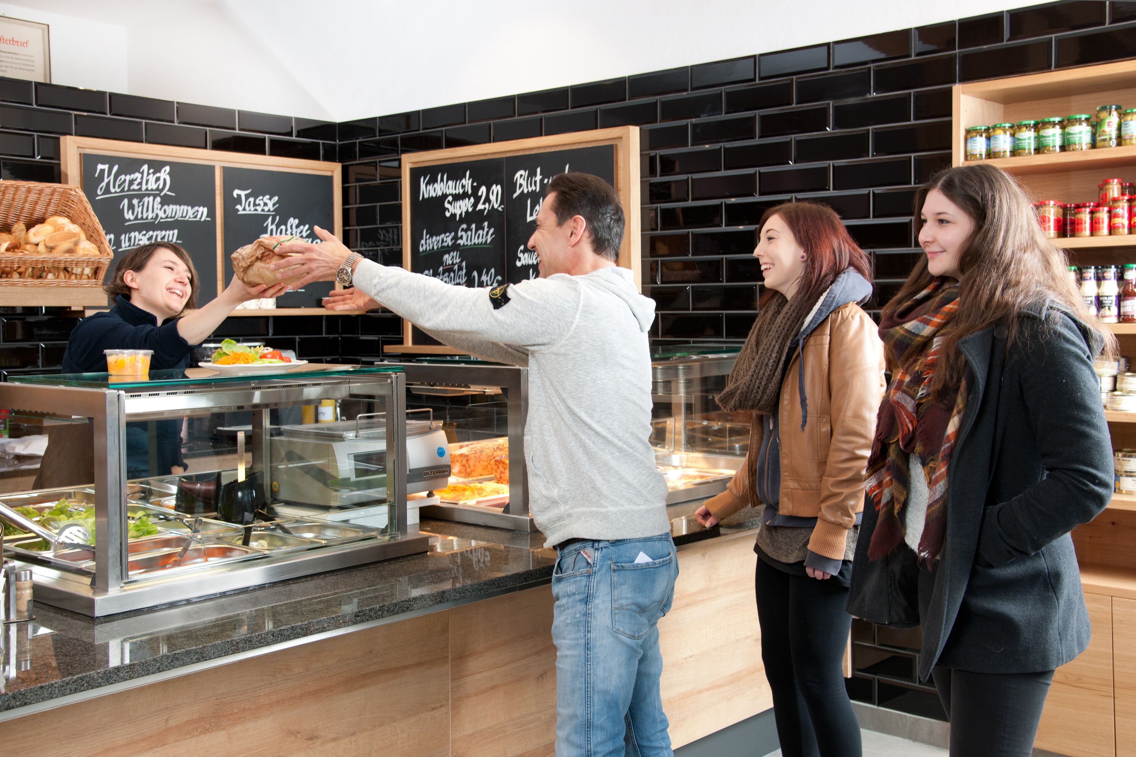Een buffetgedeelte met diverse gerechten, een krijtbordmenu en een assortiment aan sauzen en toevoegingen op planken.