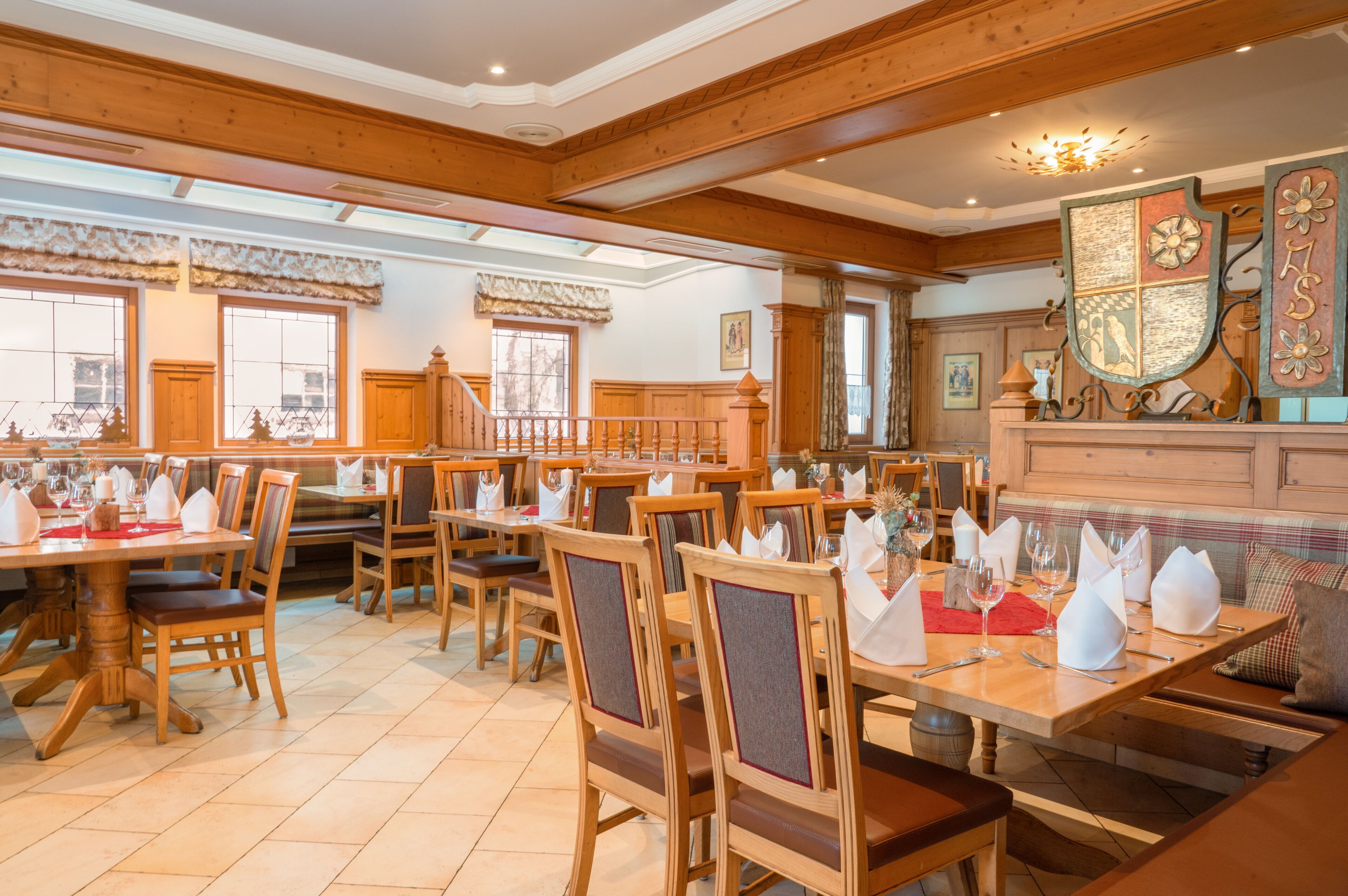 A dining area with wooden tables and chairs, a staircase, and a decorative shield on the wall.