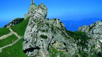 A mountain with a church on top, a bus on a road, and a clear blue sky.