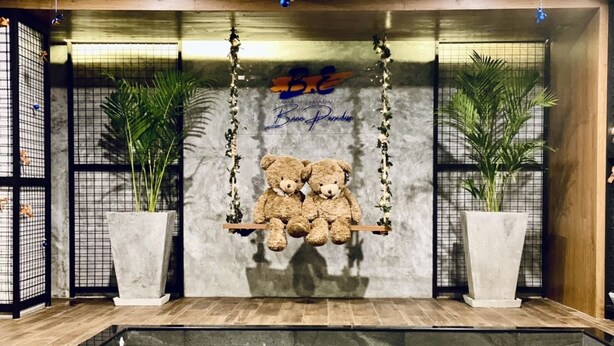 A room with a swing bed, two potted plants, a pool, and a sign reading "B.E. Beach Paradise". - BE Rendez Vous Hotel (Patong)