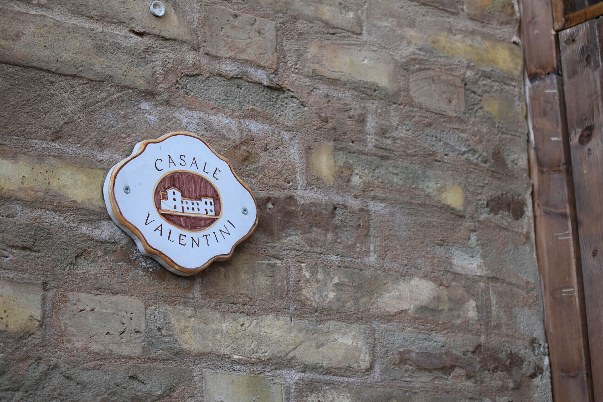 A wooden plaque with the text "CASALE VALENTINI" on a stone wall.