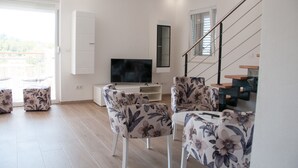 Una sala de estar moderna con un televisor de pantalla plana, sillones de estampado floral, un mueble blanco para entretenimiento y una escalera.