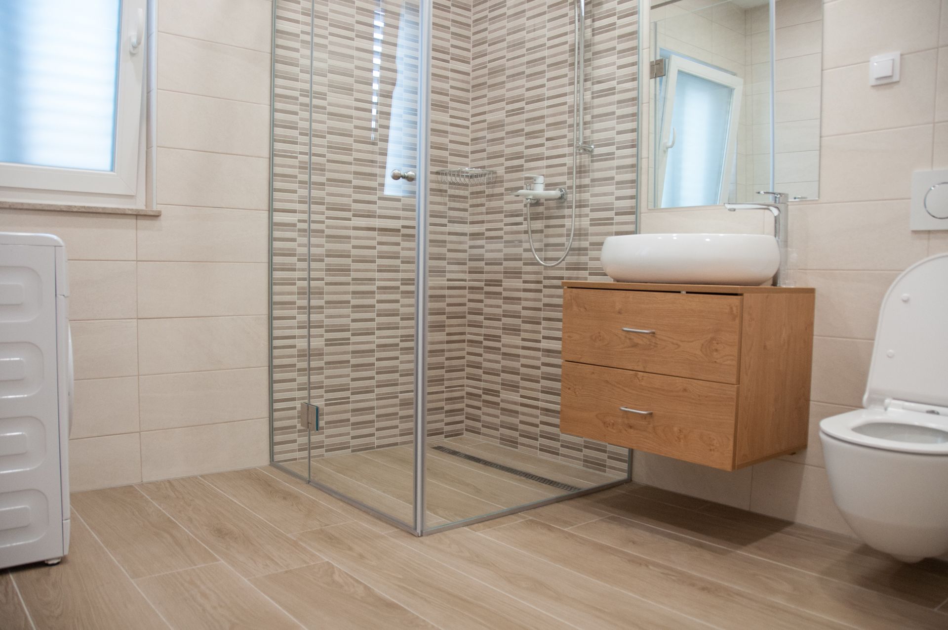 Een moderne badkamer met een douchecabine van glas, een houten wastafelmeubel met een wastafel en een toilet.
