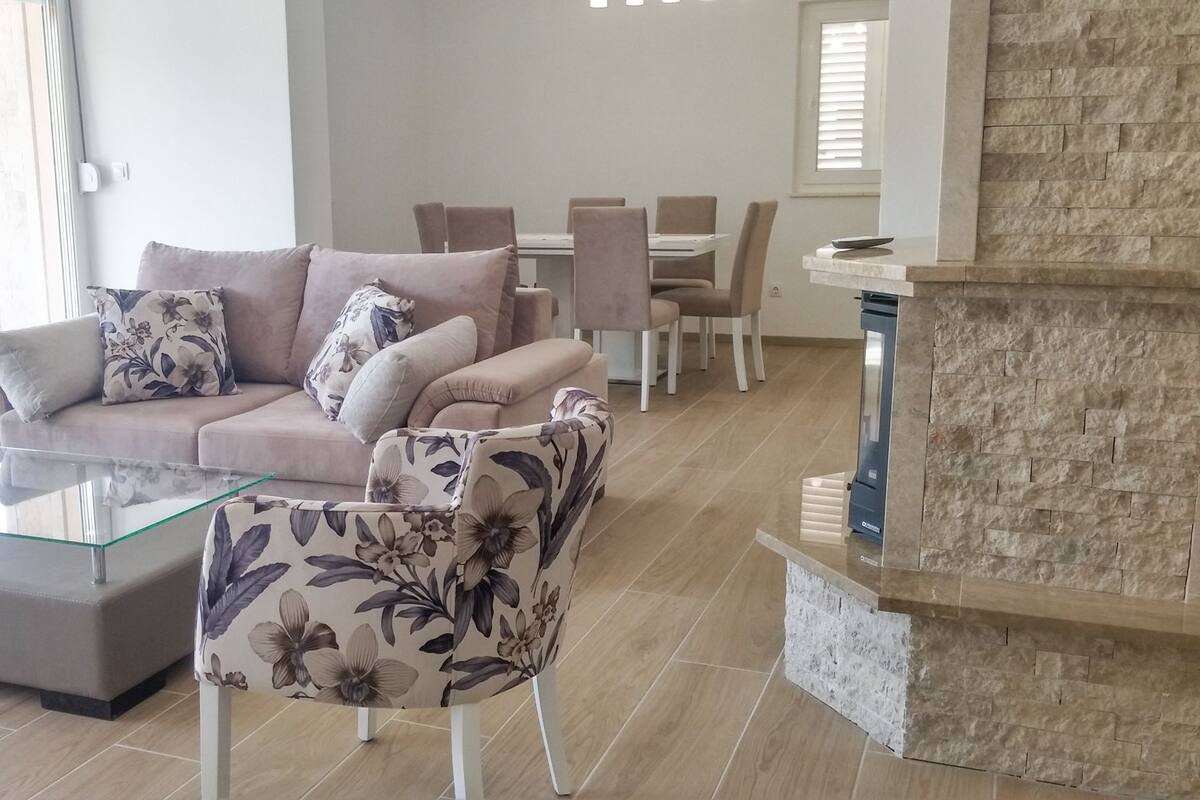 A modern living room with a glass coffee table, floral-patterned sofa, and a stone fireplace.
