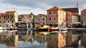 Un puerto con barcos amarrados, edificios con tejados rojos y un reflejo en el agua.