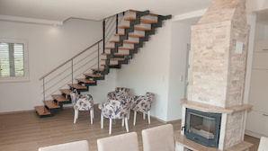 Una sala de estar moderna con una escalera de madera, una chimenea de piedra y sillones con estampado floral.