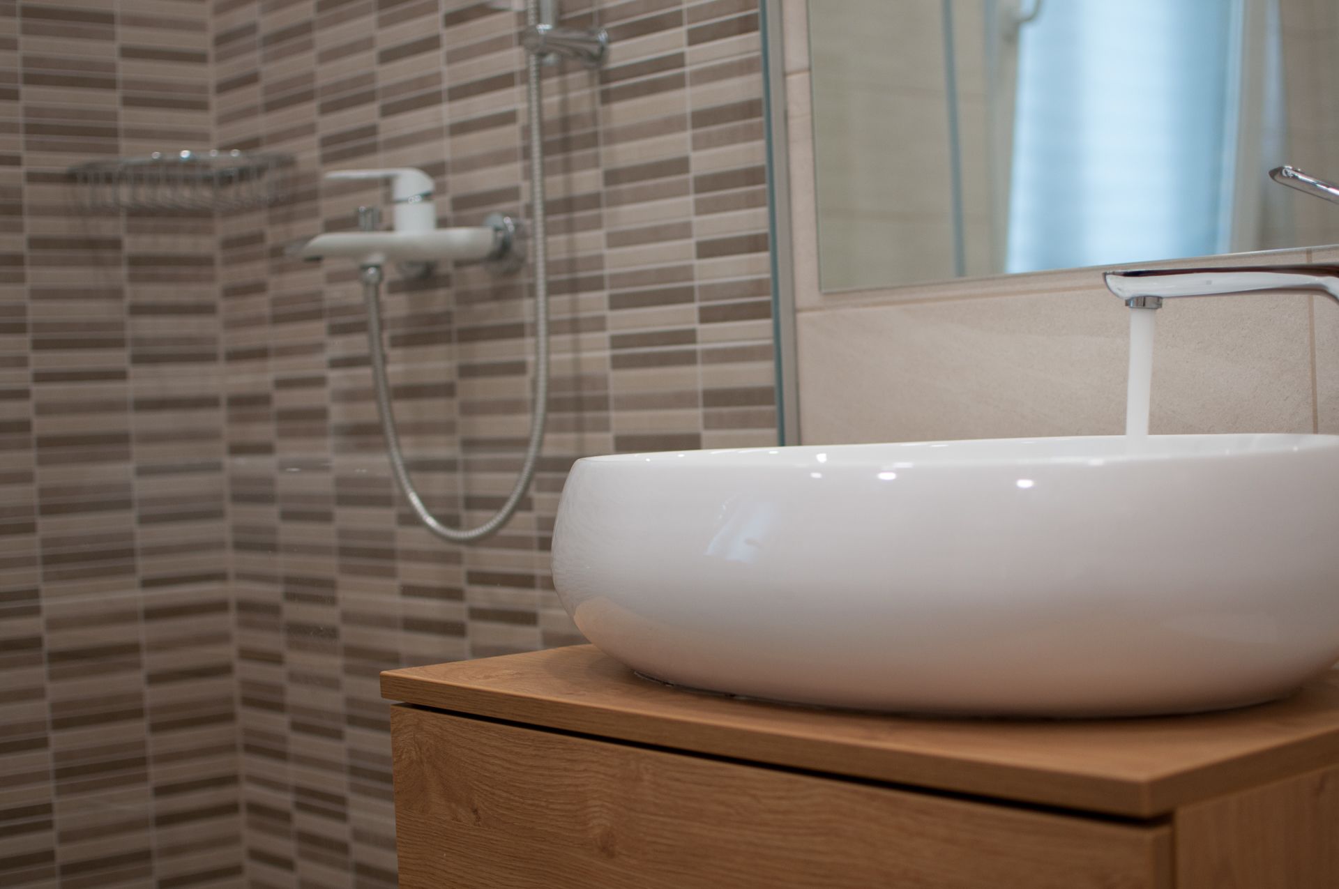A bathroom with a white sink on a wooden vanity, a mirror above the sink, and a shower with a glass door.