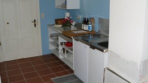 Une cuisine de taille réduite avec des meubles blancs, un plan de travail en bois et un évier. On peut y voir divers ustensiles de cuisine et des bouteilles posés sur le plan de travail.