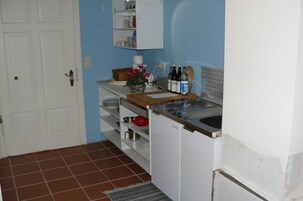 A compact kitchen with white cabinets, a wooden countertop, and a sink. There are various kitchen items and bottles on the counter.