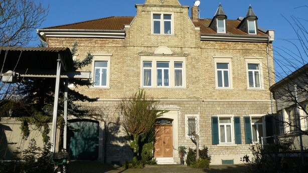 Un grand bâtiment en pierre à deux étages, doté d’une façade symétrique, de nombreuses fenêtres et d’une entrée centrale.