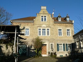 A large, two-story stone building with a symmetrical facade, multiple windows, and a central entrance.