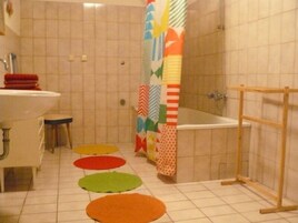 A bathroom with a white sink, toilet, and bathtub. There are colorful mats on the floor and a shower curtain with various patterns.