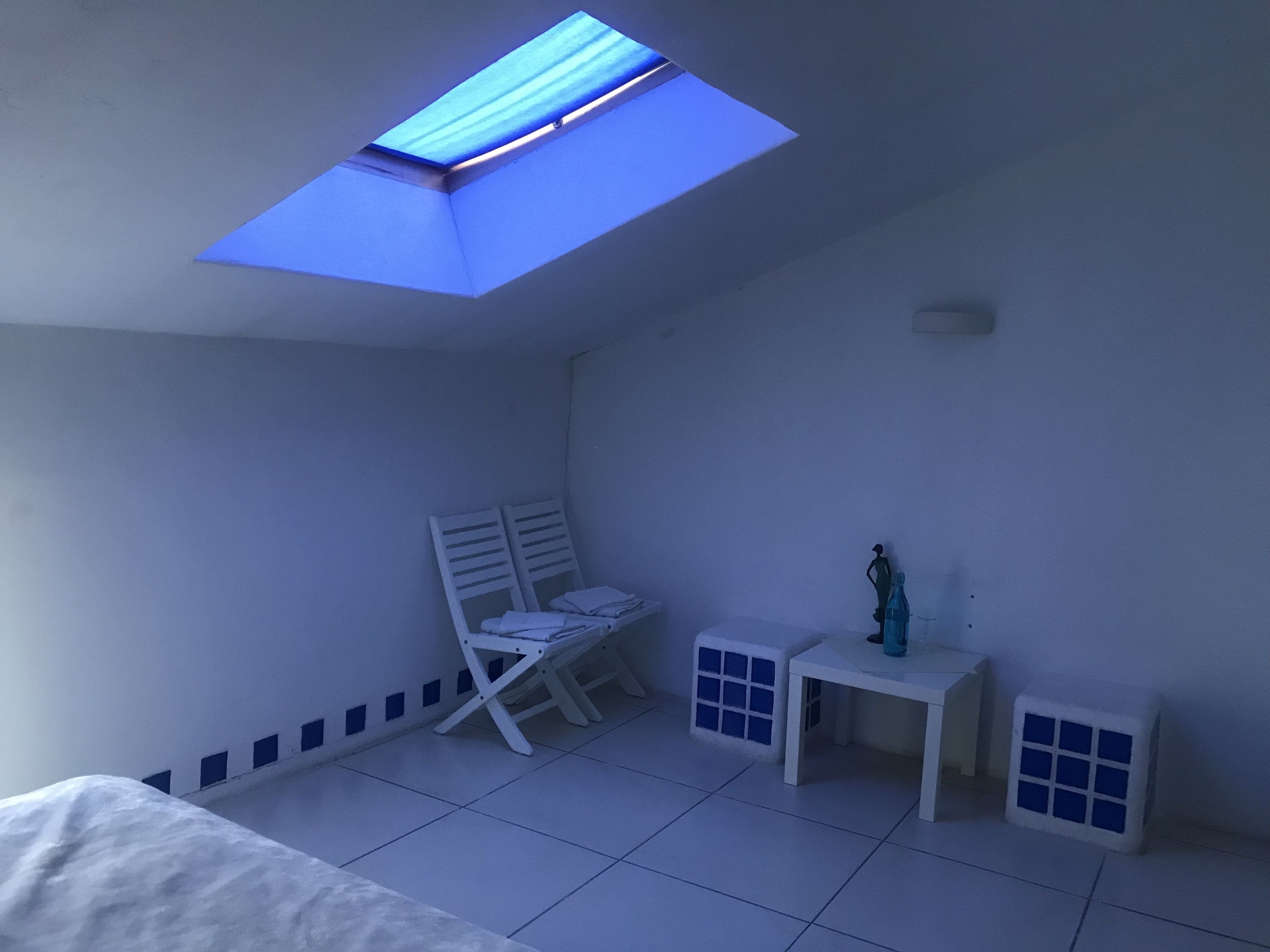 Ein Zimmer mit Oberlicht, einem Bett, einem Sessel, einem kleinen Tisch und einem Fenster.
