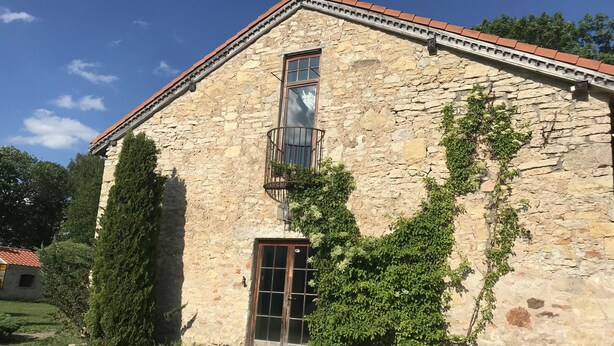 Un edificio de piedra con techo de tejas, puerta de madera y ventana con balcón de metal.