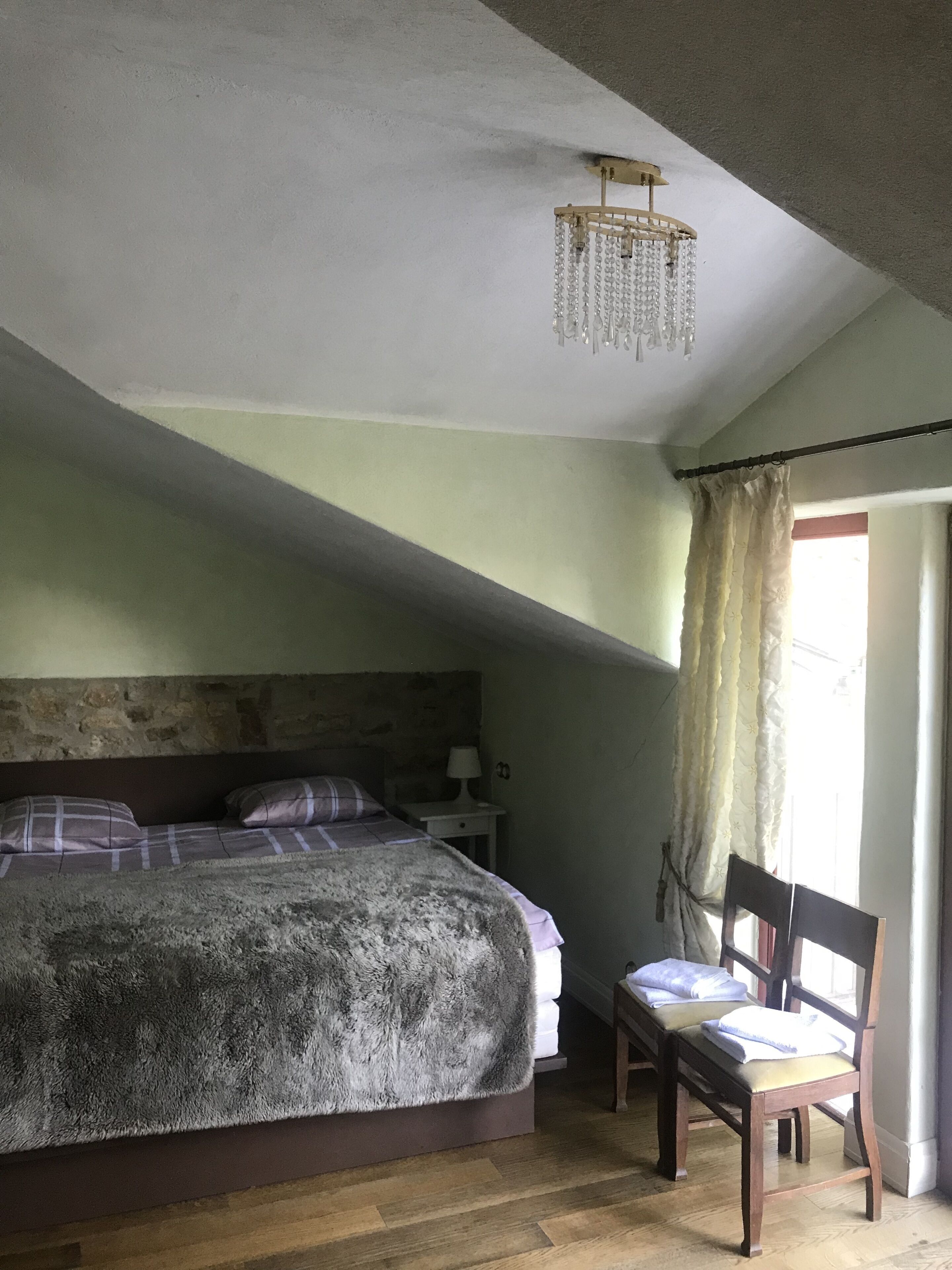 Een slaapkamer met een bed, een stoel, een nachtkastje, een lamp en een raam met gordijnen.
