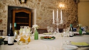 Mesa de comedor dispuesta con botellas de vino, copas y un candelabro en una habitación con paredes de piedra.