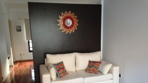 A white sofa with colorful throw pillows in a room with wooden flooring and a dark accent wall. - Beautiful bright apartment located in the best area of Palermo with 2 bathrooms! (CABA)