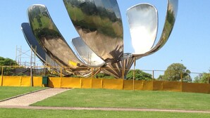 A large metallic sculpture with multiple curved surfaces, set in a grassy area with a yellow fence and some scaffolding in the background. - Beautiful bright apartment located in the best area of Palermo with 2 bathrooms! (CABA)