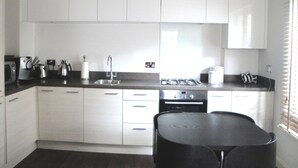 Uma cozinha moderna com armários brancos, bancada preta, pia, fogão e mesa de jantar preta.
