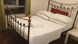Cama bem arrumada com lençóis brancos e almofadas vermelhas, cabeceira de metal e escada de madeira.