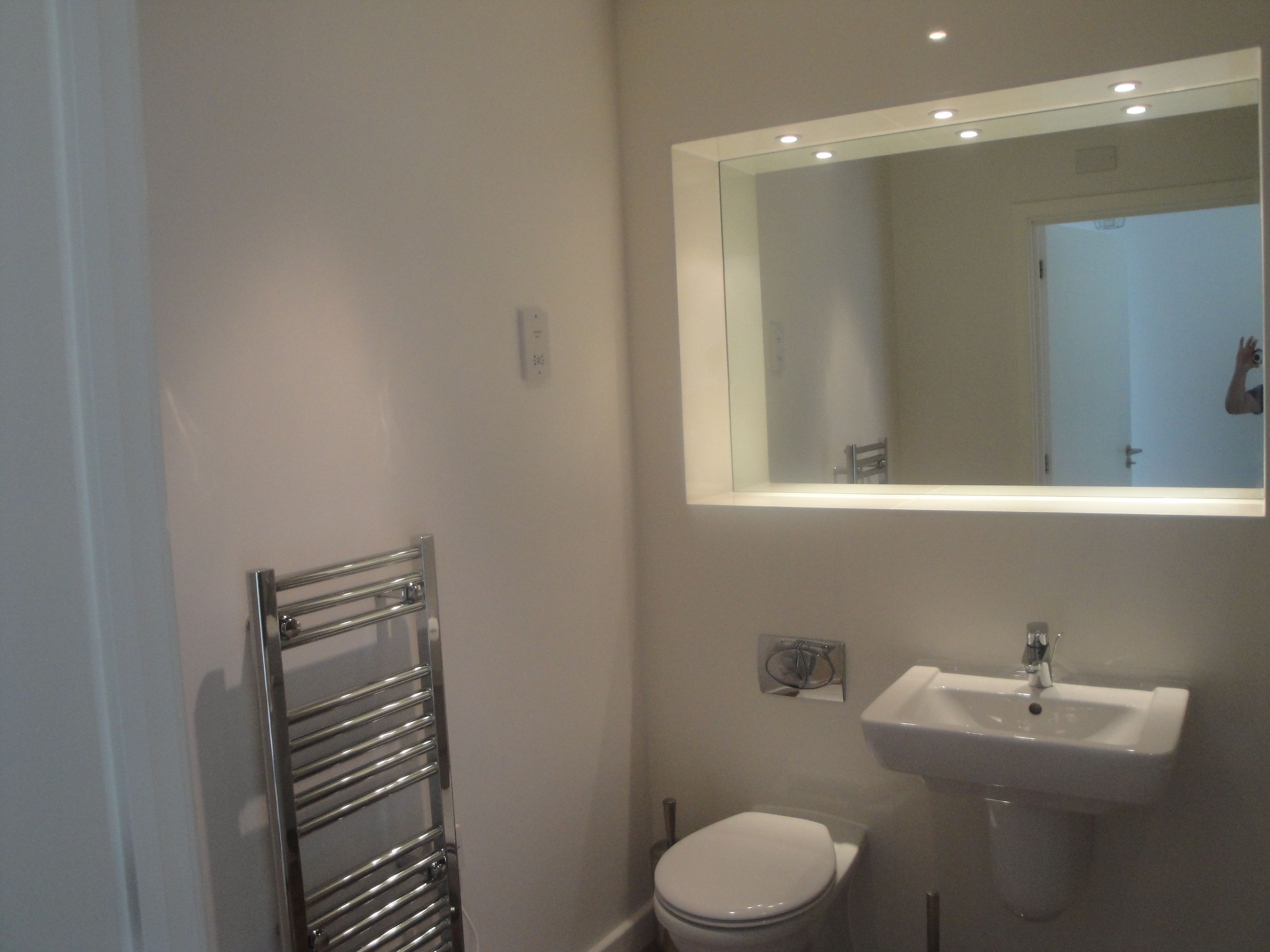 A modern bathroom with a white toilet, a chrome towel rack, a white sink, and a mirror above the sink.
