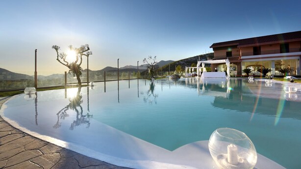 A clear pool with a glass bottom, surrounded by a paved area and a building with a balcony. - Masseria Nobile (Fisciano)