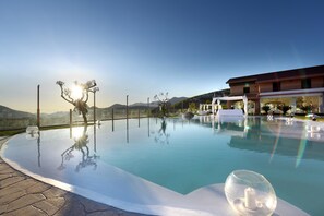 A clear pool with a glass bottom, surrounded by a paved area and a building with a balcony. - Masseria Nobile (Fisciano)