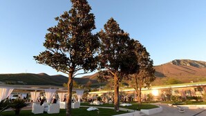 An outdoor event space with white tents and tables, surrounded by trees and a building with a green roof. - Masseria Nobile (Fisciano)