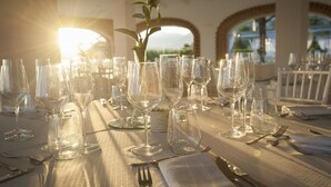 A table set for a meal with multiple wine glasses and cutlery, a potted plant, and a view of the outdoors through an arched window. - Masseria Nobile (Fisciano)