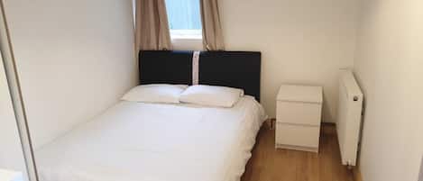 Una cama pequeña y bien hecha con ropa blanca en una habitación compacta.