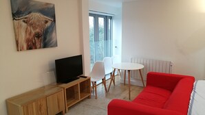 A modern living room with a red sofa, a TV on a wooden stand, a dining table with chairs, and a large window. - Awesome City Apartment (Cambridge)