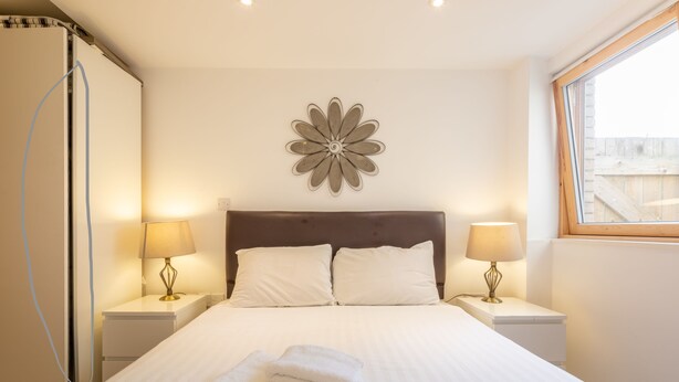 A hotel room with a large bed, two bedside lamps, a decorative wall piece, and a window with a view. - Awesome City Apartment (Cambridge)