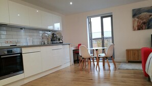 A modern kitchen with white cabinets, a Bosch oven, and a dining area with a table and chairs. - Awesome City Apartment (Cambridge)