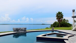 Piscina com vista para a água, uma rocha e uma palmeira.