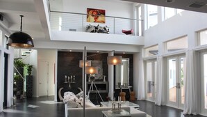 Uma sala de estar ampla com pé direito alto, área de estar central e escada que leva a um andar superior.