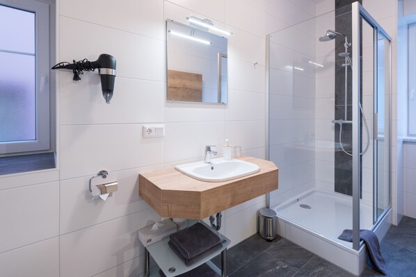 Un baño moderno con tocador de madera, cabina de ducha con mampara de cristal y un espejo grande.